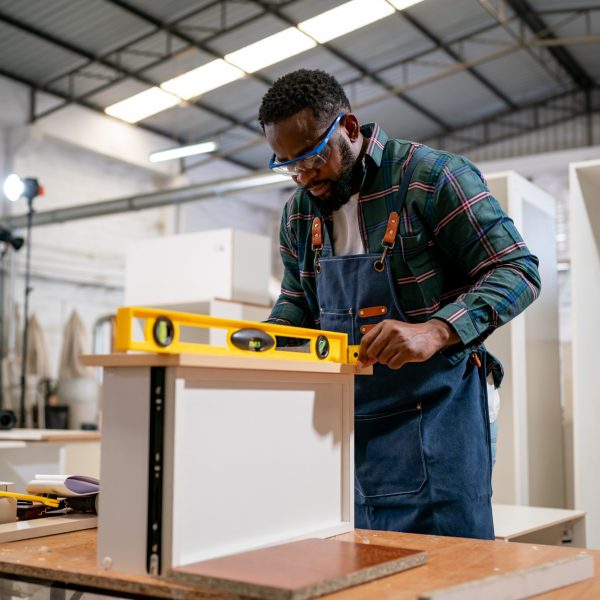 Manual worker using sander while working on a wood in carpentry workshop.